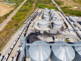 Industrial storage facility near railway tracks with silos and trains in the background during daytime © DSMT
