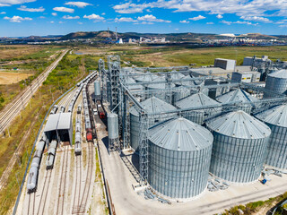 Large storage silos and train tracks in an agricultural area with mountains in the background © DSMT