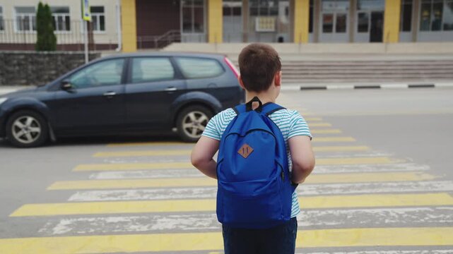 Young pedestrian, Blue schoolbag, Child waiting patiently, School is close, Watching the road, Cars on the street, Crosswalk safety, Everyday school commute, City lifestyle, Following traffic rules,