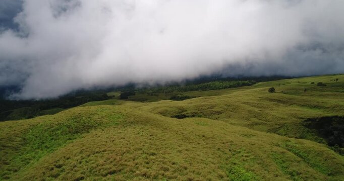 Aerial drone view of green savanna hills with low clouds rolling over ridges, Mount Rinjani trekking route, Lombok, Indonesia.
