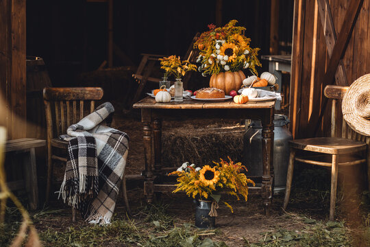 Cozy autumn composition near old wooden country house. Table setting for family thanksgiving dinner with homemade apple pie, bouquet of sunflowers, pumpkins. Elegant rustic cottage core home decor