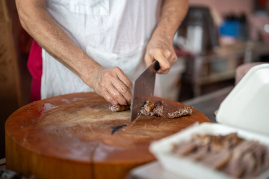 Vendor cutting fried pork meat and selling takeaway meals for customers at street food market in Bangkok, local seller slicing cooked meat preparing portions for containers at food market in Thailand.