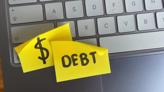 Debt and dollar sign sticky notes on laptop keyboard finance concept