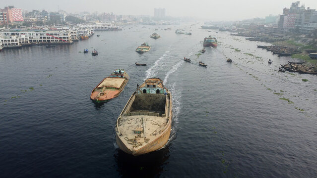 Aerial view of the Buriganga River featuring various cargo boats and vessels navigating the waterway amidst the urban landscape of Dhaka, Dhaka Division, Bangladesh.