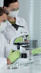 Scientists collaborating in a medical research laboratory, using a brightfield microscope to...