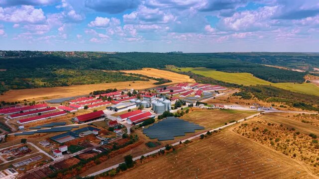 Industrial complex scattered in the wilderness. Large agricultural facility with red-roofed warehouses. Fluffy clouds in the sky above.