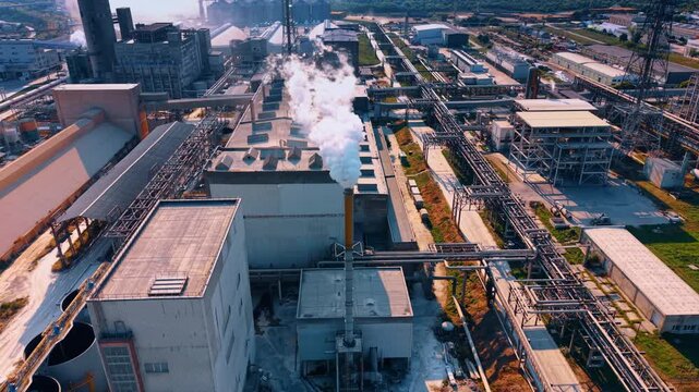A large-scale production facility with dense pipelines and warehouses. Drone flight over the industrial plant at daytime.