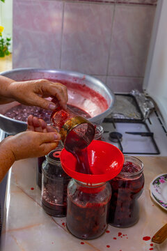 Hands Pouring Homemade Strawberry Jam into Glass Jars