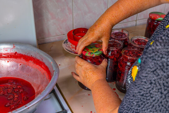 Hands Sealing Jars of Homemade Strawberry Jam in Kitchen
