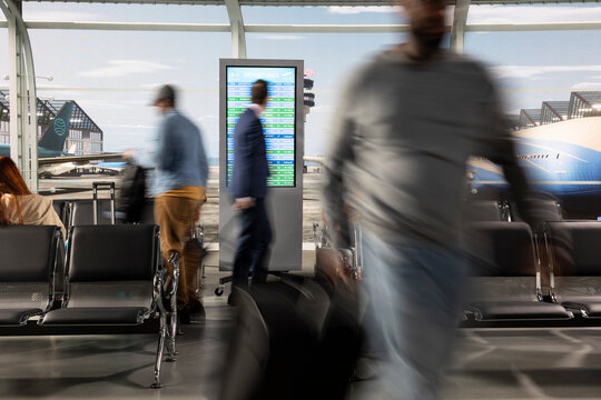 Blurred travelers reading electronic flight timetable at airport