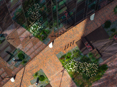 Aerial view of a modern self-sufficient office building featuring a glass facade, brick-paved courtyard, lush green landscaping, and bike racks in Poland.