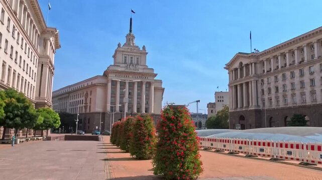 Sofia, Bulgaria - 10.09.2026, Front architectural view of the National Assembly, former Communist Party House, red flower bushes along the road.