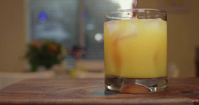 Red fruit juice pouring into an orange cocktail over ice