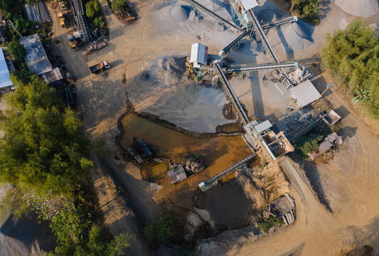 Aerial view of a sand and gravel processing facility with conveyor belts, stockpiles of aggregate, and muddy water in Cilongok, Central Java, Indonesia.