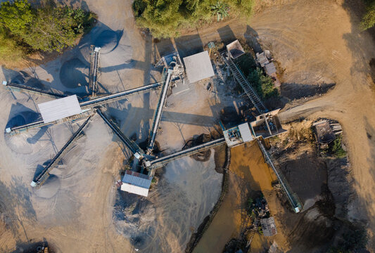 Aerial view of a stone crushing plant with conveyor belts, piles of gravel, and muddy water in Cilongok, Central Java, Indonesia.