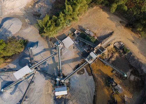 Aerial view of a stone crushing plant with conveyor belts, piles of gravel, and industrial machinery in a rural landscape in Cilongok, Central Java, Indonesia.