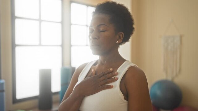 Woman with hand on chest and closed eyes practicing breathwork in a yoga studio; serenity mindfulness.