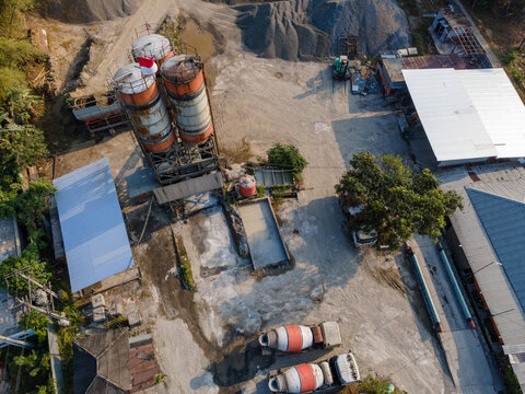 Aerial view of a concrete batching plant featuring industrial silos, cement mixer trucks, gravel piles, and storage buildings in Cilongok, Central Java, Indonesia.