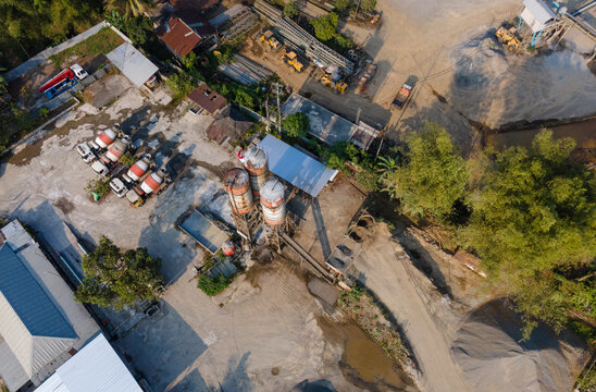 Aerial view of a concrete batching plant with cement silos, mixing trucks, and piles of gravel in an industrial site in Cilongok, Central Java, Indonesia.