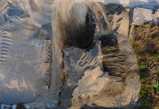 Aerial view of a sand mining site with large piles of excavated earth and sand, showing textured ground patterns and tracks in Cilongok, Central Java, Indonesia.