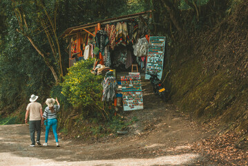 Fototapeta premium Hikers walking along a forest trail beside a small roadside souvenir stall, combining outdoor adventure, tourism and local commerce.