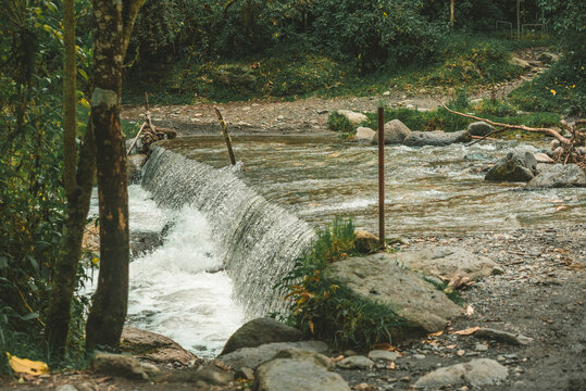Rocky river flowing through dense forest with a small waterfall, creating a peaceful freshwater landscape for nature tourism and outdoor recreation.