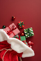 Naklejka premium Santa Claus gifts spilling from red sack with wrapped Christmas presents and ornaments for Merry Christmas Happy New Year on vertical burgundy space