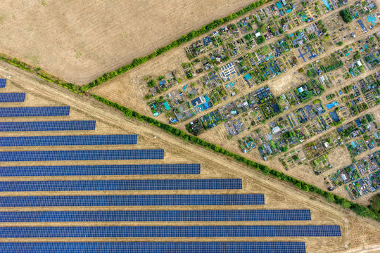 Aerial view of solar farm panels arranged in rows adjacent to a residential allotment area with small garden plots and paths in Hook, England, United Kingdom.