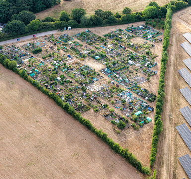 Aerial view of an allotment garden area with small plots and sheds situated next to a solar farm in the countryside of Hook, England, United Kingdom.
