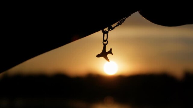 Airplane pendant dangles gently in slow motion against a bright golden hour sun. Warm silhouette composition provides compelling visual assets for travel and airline ads.