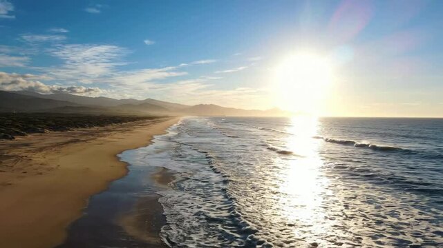 Aerial view of golden sunset over tropical beach with gentle ocean waves and mountain horizon drone
