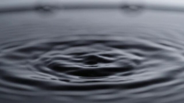 Slow motion water drop impact creating concentric ripples on dark liquid surface splash