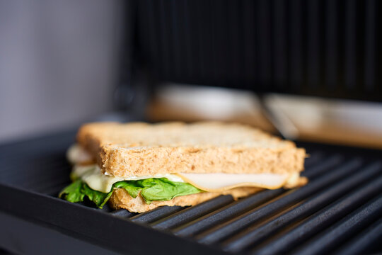 Sandwich with cheese, lettuce and sliced meat placed on open electric grill