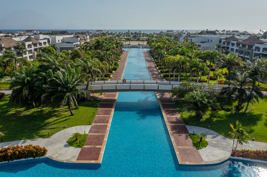 Aerial view of Hard Rock Hotel Casino Punta Cana with a long pool, pedestrian bridge, palm trees, and manicured lawns in Punta Cana, La Altagracia, Dominican Republic.