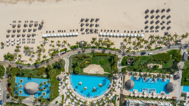 Aerial view of Hard Rock Hotel Casino Punta Cana featuring swimming pools, lush gardens, palm trees, and sandy beach with rows of umbrellas in Punta Cana, La Altagracia, Dominican Republic.