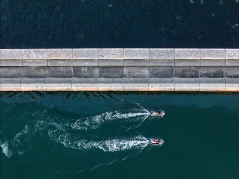 Aerial view of two jet skis leaving white wakes as they travel through deep blue water alongside a concrete pier in Cascais, Lisboa, Portugal.