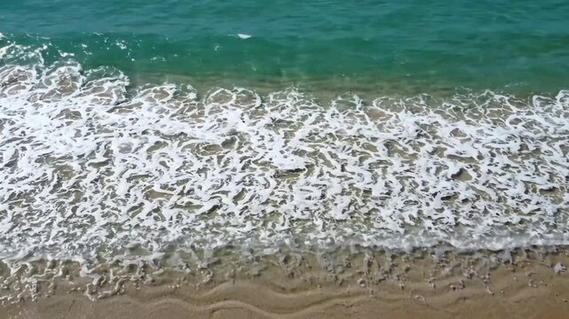 Crystal clear ocean waves gently rolling onto sandy beach shoreline