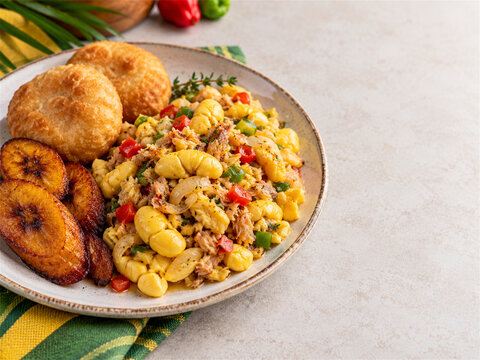 Traditional jamaican ackee and saltfish breakfast served with fried dumplings sweet plantain and colorful vegetables on a rustic plate with bright natural food styling and generous copy space