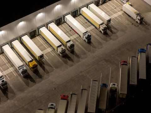 Aerial view of semi-trucks parked at a logistics warehouse loading dock at night in Gdansk, Poland.