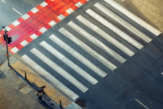 Aerial view of a pedestrian crosswalk with a red-painted lane and a person walking on the sidewalk in Warsaw, Poland.