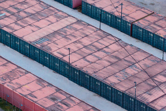 Aerial view of rows of weathered shipping containers with red tops and dark blue sides arranged in a storage yard in Warsaw, Poland.