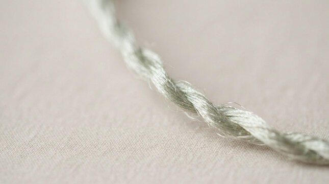 Twisted natural fiber rope with white and green strands on neutral textile background