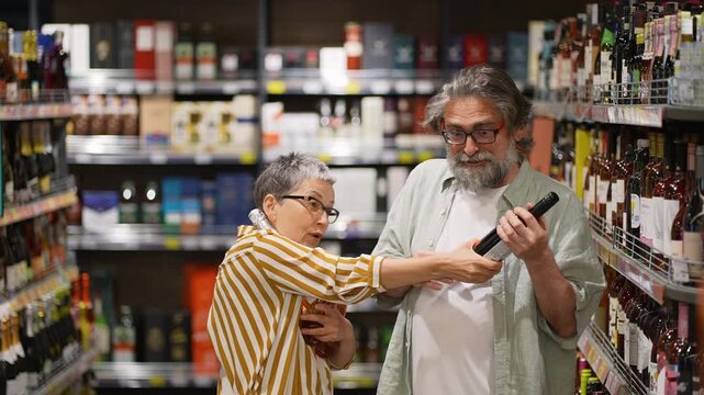 Mature couple arguing while choosing wine in supermarket aisle