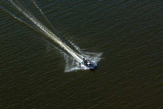 Aerial view of a fast fishing motor boat speeding across dark water, leaving a white wake behind it in Poland.