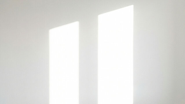 Two vertical window light shadows on a blank white wall