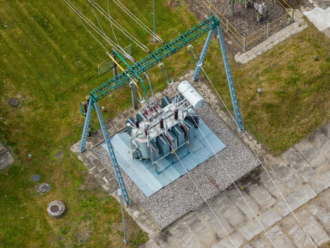 Aerial view of an electrical substation featuring a large transformer and metal gantry structure set on a gravel base surrounded by green grass in Poland.