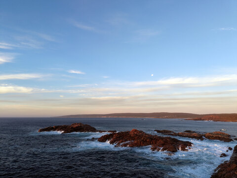 Aerial view of Canal Rocks with rugged granite formations surrounded by crashing waves and deep blue ocean under a soft sunset sky in Busselton, Western Australia, Australia.