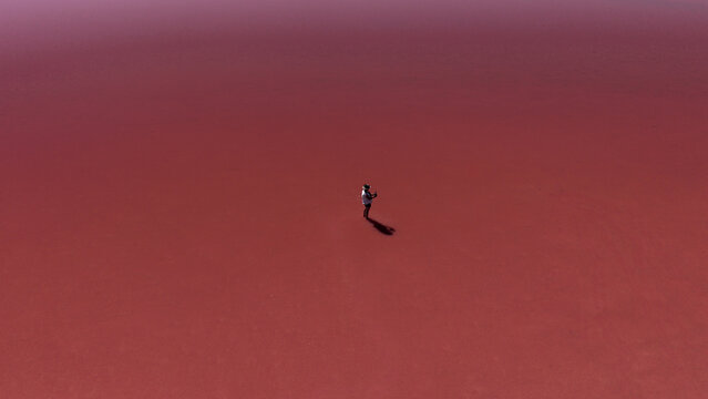 Aerial view of a person standing in the middle of the vibrant pink waters of Hutt Lagoon, Yallabatharra, Western Australia, Australia.