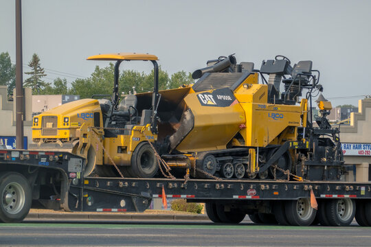 Calgary, AB, Canada - Sept 15, 2026: Yellow CAT asphalt paver and road roller loaded on a heavy flatbed trailer outdoors.