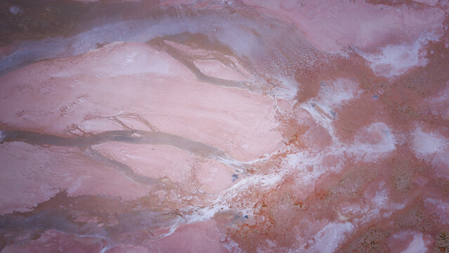 Aerial view of the vibrant pink salt flats of Hutt Lagoon, showcasing intricate patterns of mineral deposits and saline water in Yallabatharra, Western Australia, Australia.